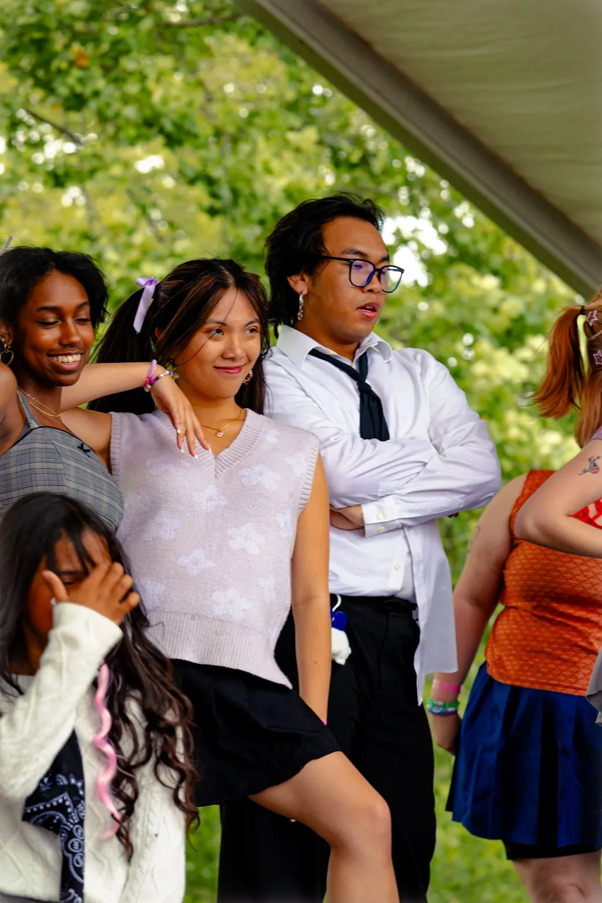 A row of young people in casual outfits stand together beneath a tent with green trees behind them at Knox Pop Con.