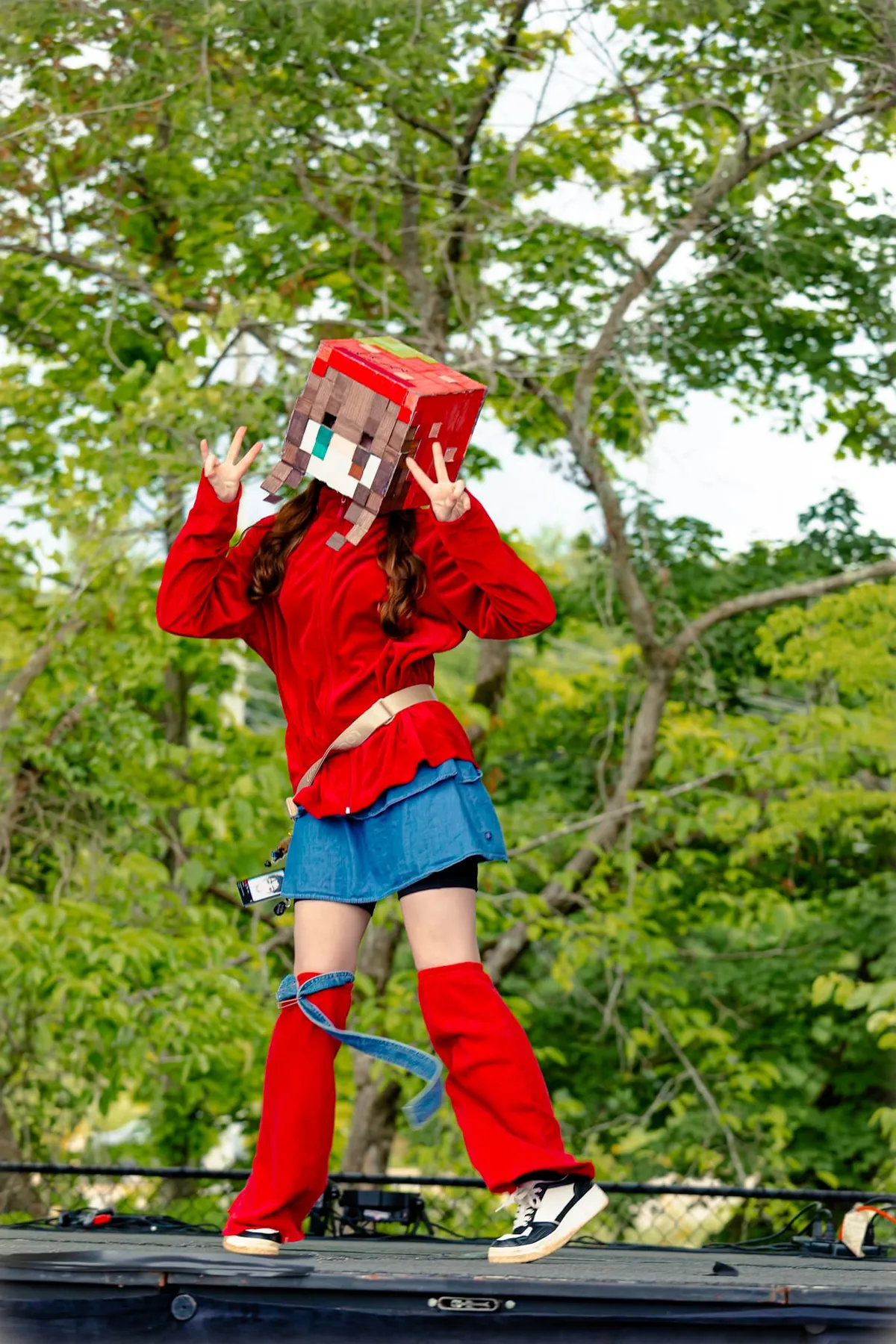 A performer in a pixelated Minecraft-style head throws double peace signs while dancing on an outdoor stage at Knox Pop Con.