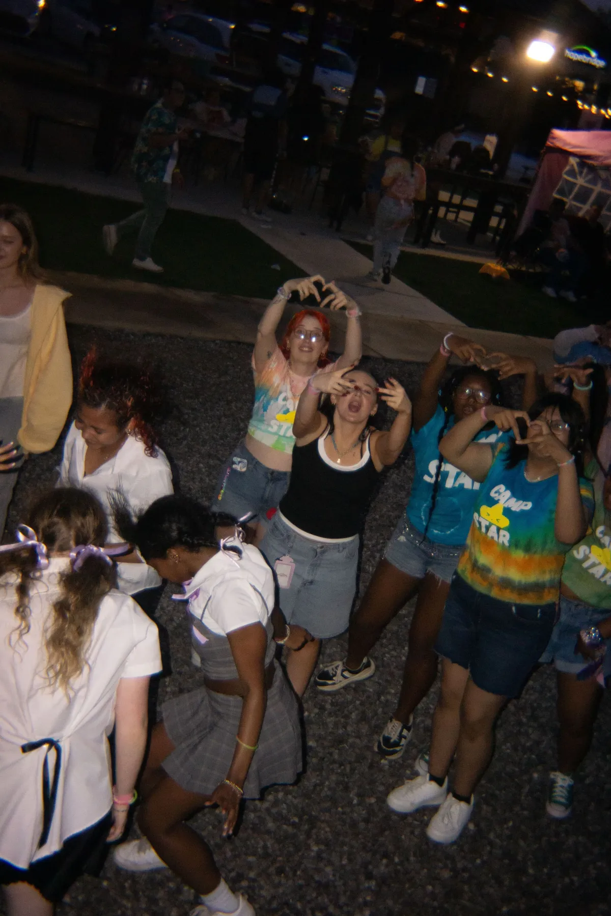 A group of attendees dance and form finger hearts under string lights at night, several wearing tie-dye Camp Star shirts, at Knox Pop Con.